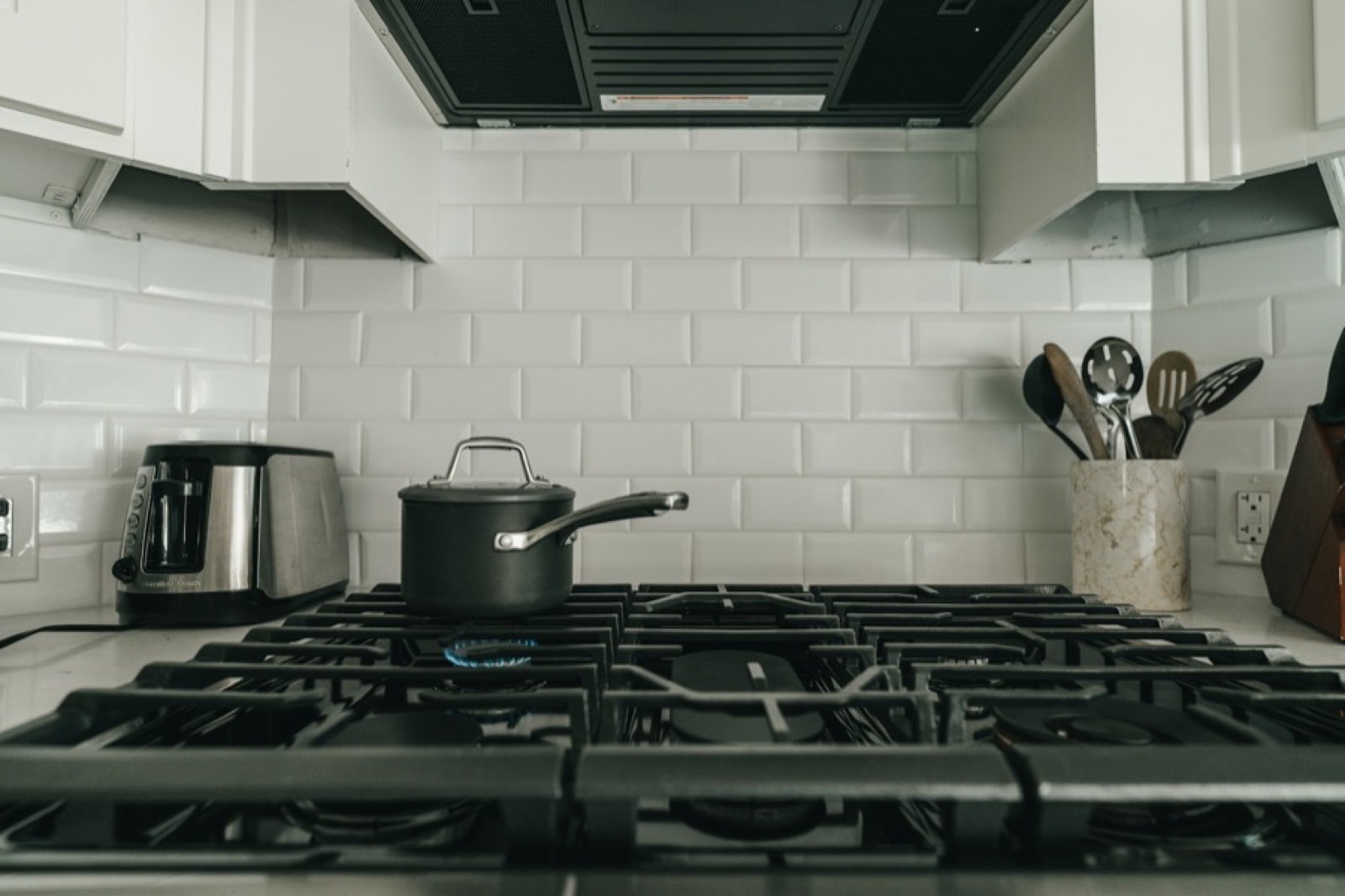 A pan on a lit gas hob with utensils beside it